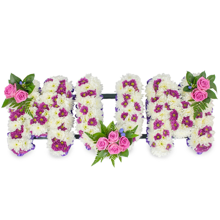 A poignant and carefully assembled floral tribute forming the word MUM, shown on a plain white background so every detail is visible. The letters are three-dimensional, each constructed from a compact, velvety mass of white chrysanthemums that give a soft, tactile quality and a tone of purity and calm. Interlaced among the white are pockets of rich magenta or deep purple spray flowers that add texture and subtle movement across the letter faces. Three clusters of pink spray roses provide the emotional focal points: a small accent at the top left of the first M, a more substantial bouquet cradled into the lower curve of the U, and a corresponding cluster at the top right of the final M. Lush dark green foliage-including feathery fern fronds-and a scattering of tiny blue accent blooms complete the palette with cool and grounding notes.
A delicate purple ribbon outlines the letters and a low-profile dark horizontal bar behind them keeps the trio united and stable when placed on a memorial easel or funeral stand. The craftsmanship is deliberate: stems are wired and trimmed so the surfaces stay seamless, the colours are balanced to read well under soft chapel lighting, and the scent is gentle rather than overpowering. This style of tribute is commonly chosen by families in the Stanmore area-from Stanmore Hill to the roads near Stanmore station and beyond-who want a personalised and dignified expression of grief and gratitude. The arrangement communicates respect, memory, and tender affection for a beloved mother with quiet refinement.