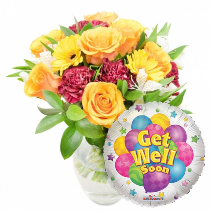A vivid, heartening Get Well Soon gift ensemble set against a simple white studio background: a full, luminous bouquet in a clear glass vase pairs with a reflective round Mylar balloon tucked to the lower right. The bouquet's architecture centres on generous orange and deep yellow roses whose spiraling petals feel warm and velvety to the touch; they are balanced by bright yellow gerbera daisies that radiate optimism, and by full-bodied burgundy carnations that bring a rich, textured contrast. Sprigs of small white alstroemeria weave throughout like threads of light, softening the composition and lending a faint, sweet perfume. Rich green foliage fills and frames the blooms, its glossy leaves giving the arrangement a fresh, lively outline while the transparent vase exposes the water and interlaced stems beneath-evidence of considered floral technique. The balloon is metallic silver and decorative: a cheerful cluster of illustrated balloons in sky blue, lilac, lime, pink and sunny yellow-with playful patterns of stripes, polka dots and checks-surrounds the prominent yellow-and-blue shaded lettering Get Well Soon. Scattered starbursts dot the balloon's white border, and the small KALEIDOSCOPE logo is visible at the very bottom. This composition reads as an encouraging bedside gift or a bright pick-me-up for someone recuperating near Canons Park, Bentley Priory or anywhere across Stanmore, carrying the gentle reassurance of a local florist's touch.