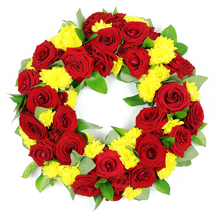 A large, circular sympathy wreath is shown in sharp detail against a stark white background, its form and colours commanding quiet attention. The wreath is entirely composed of red and yellow blooms, most prominently deep red roses and bright yellow chrysanthemums, woven together in a dense, continuous ring. Each rose appears at the peak of its beauty, with velvety petals arranged in elegant spirals, the tones shifting subtly from rich crimson at the core to deeper burgundy shadows along the folds, suggesting depth and tenderness. Nestled between these roses are groups of yellow chrysanthemum heads, their many slender petals forming small, fluffy domes that soften the overall look and introduce a warm, uplifting glow. Anchoring the design is an abundance of greenery: broad, glossy leaves that reflect the light, along with finer, cooler foliage in silvery green, reminiscent of eucalyptus or similar textural greens frequently used by experienced florists in Stanmore. This foliage peeks through the flowers just enough to add contrast and volume without distracting from the bold red and yellow palette. The circle itself is meticulously shaped, with an even thickness all the way around and a clean, open centre, symbolising continuity and the lasting nature of cherished memories. The bright, even studio-style lighting ensures every petal edge, leaf vein, and colour gradient is visible, making the wreath feel almost tangible. Designed as a funeral or memorial tribute for services around Stanmore, this arrangement conveys deep love, respect, and a gentle sense of hope, honouring a life with both solemnity and warmth.