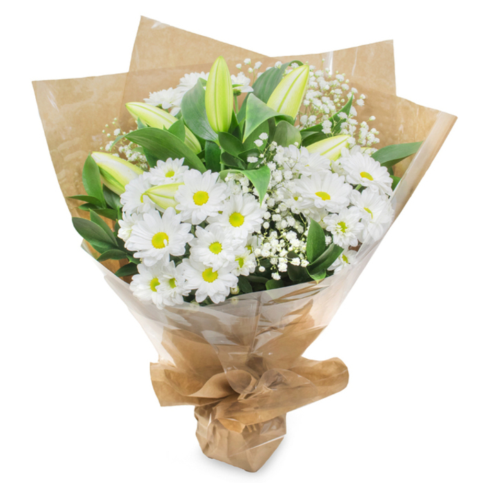 A gentle, hand-tied bouquet of white and green flowers is displayed upright against a clean white background, with no distractions from its composed, peaceful beauty. At the centre, many daisy-like chrysanthemums in pure white are packed closely together, each flower formed from layers of slender petals radiating around a bright yellow-green disc. These cheerful centres lend a subtle touch of life and warmth without disturbing the bouquet's quiet, respectful mood. Emerging from this bed of daisies, tall lily buds stretch upwards, their petals still firmly closed, smooth and sleek to the eye, with tones moving from light green at the base to creamy white at the tips. Their presence brings a sense of future bloom and unfolding remembrance. Fine sprays of white baby's breath, or gypsophila, are scattered between the main flowers, their tiny clustered blossoms creating a soft, airy halo, almost like a veil of light encircling the arrangement. Around the edge, rich dark green foliage forms a solid frame; the leaves, glossy and slightly pointed, provide depth and structure, grounding the bouquet so it feels calm and complete. The stems are wrapped first in brown kraft paper, its natural, slightly crumpled texture giving the design a modest, down-to-earth character, reminiscent of simple tributes carried to services in and around Stanmore and Harrow Weald. Over this sits a transparent layer of cellophane, lightly reflecting the light and keeping the flowers in perfect condition for local delivery. Everything is drawn together and tied securely at the base, forming an easy-to-hold, conical bundle. The overall impression is of purity, serenity, and quiet strength, making the bouquet an ideal choice for sending sympathy, marking a farewell, or offering gentle comfort to loved ones in Stanmore.