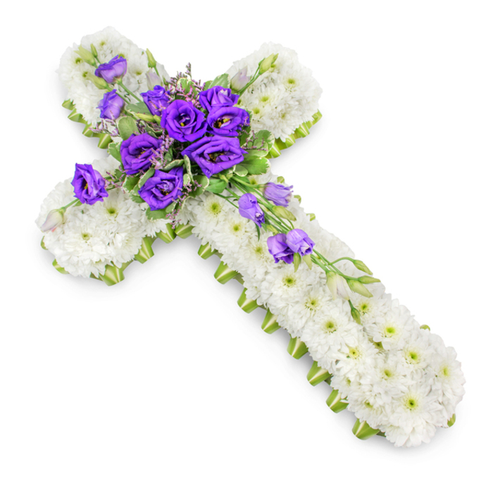 A beautifully detailed floral cross, created as a Christian sympathy tribute, is presented on a bright white backdrop that enhances its purity and structure, reminiscent of arrangements resting near altars in Stanmore's local churches. The cross is entirely carpeted with small white spray chrysanthemums, so closely arranged that they form a smooth, almost quilted surface. Their petals are soft and slightly ruffled, overlapping to create depth and a gentle, tactile texture. Tiny hints of pale green at the centres of the blooms add a whisper of colour, giving the white a fresh, living quality. Encasing the cross is a slender ribbon of lime green that follows every curve and angle of the outline. This delicate border defines the shape with precision, its subtle sheen catching the light and offering a modern contrast to the traditional floral base, much like a touch of new foliage along the paths of Stanmore Country Park. At the crossroads of the vertical and horizontal arms, a lush cluster of deep purple lisianthus draws the eye immediately. The flowers vary in size and openness, with some tightly budded and others fully open, revealing their rich, velvety petals folded in soft layers. Intermingled among them are strands of light green foliage and small filler flowers that soften the mass of purple, blending it gently into the sea of white chrysanthemums. From this central gathering, several lisianthus stems extend gracefully along the lower arm of the cross, their blooms and buds arranged in a gentle, cascading line that creates a sense of movement and flow. The lighting is even and softly diffused, revealing every detail and casting only a delicate shadow beneath the cross, as though it is resting lightly on a table or easel. The overall mood is one of reverence, peace, and heartfelt condolence, making this floral cross a fitting tribute for funerals and memorial services throughout Stanmore.