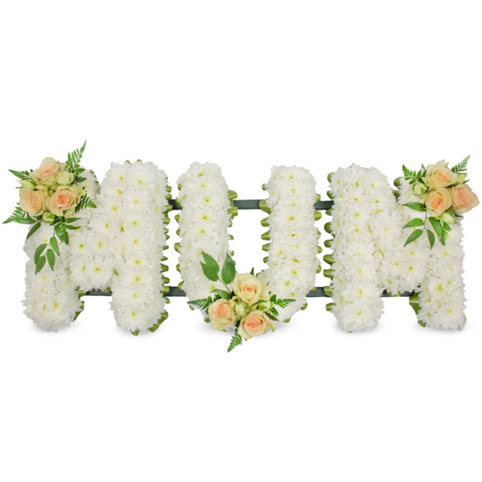In this detailed floral tribute, the word MOM is spelled out in large, bold capital letters that stretch horizontally across the image, resting against a spotless white background that gives the arrangement a clean, contemporary feel. Each letter is densely packed with pristine white flowers, likely spray chrysanthemums or similar small-headed blooms, placed so close together that they form a thick, cushiony bed of petals. The soft, layered texture of the flowers suggests comfort and serenity, making the piece particularly suitable for a funeral or memorial in Stanmore, where families gather to reflect and remember. A supportive dark green frame and slim ribbon edge subtly trace the outline of each letter, providing structure and ensuring that the word remains clearly legible even from a distance in a church or crematorium chapel. To bring warmth and a more personal touch, three clusters of soft peach and apricot spray roses are carefully nestled into the design. One cluster adorns the upper left curve of the first M, another sits gently at the bottom centre of the O, and the final cluster accents the upper right curve of the second M, mirroring the first for balance. The roses, some in tight bud and others softly opening, are surrounded by sprigs of feathery fern and rich green foliage that give depth, contrast, and a sense of natural garden beauty reminiscent of local green spaces like Canons Park and Stanmore Country Park. The overall impression is one of quiet dignity and heartfelt love, an arrangement created with the understanding that flowers can speak when words are difficult. Crafted with care by Flowers Stanmore for local families, this MOM tribute honours a mother's memory with purity, grace, and an unmistakably tender presence.