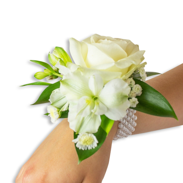 This refined wrist corsage is captured from a slightly elevated angle, the pale-skinned wrist angling into a minimalist white background so the composition's details are easy to study. Dominating the arrangement is a fully opened creamy white rose, its center tight and petals unfolding in delicate, velvety waves that suggest both tenderness and formality. Below it, offset to the left, a trumpet-shaped white bloom - with subtle ribbing and a pale green-yellow throat reminiscent of alstroemeria - offers sculptural contrast and draws the eye inward. Interspersed among these primary flowers are several small, green-tinged buds that lend structure and an anticipatory note, while clusters of fine Baby's Breath weave through the design, creating soft, diffused highlights. At the lower left, tiny daisy-like white florets with golden centers punctuate the composition with a charming, almost nostalgic accent. The arrangement is anchored by broad, glossy dark-green leaves whose smooth, waxy texture frames the petals and provides a rich, living backdrop. Securing the floral grouping to the wrist is a tasteful multi-strand pearl bracelet - the beads are uniformly round, satiny, and elastic, offering both comfort and a classic decorative band. The overall impression is one of measured elegance: the cool lustre of pearls, the quiet perfume of fresh blooms, and the balanced interplay of white and green make this corsage a perfect choice for formal ceremonies, proms, and wedding parties where refined detail matters.