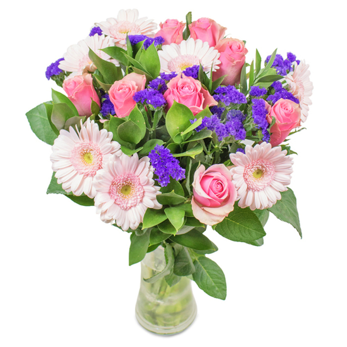 A refined bouquet sits gracefully in a transparent glass vase, stages against a pristine background reminiscent of the light-filled interiors of Stanmore homes. At the centre, seven to nine pink roses reveal themselves in varying stages of bloom: some tightly furled, others unfurling into classic spirals, their hues ranging from soft to medium pink-like the blush of dusk over Stanmore Hill. Encircling these are five to seven pale pink gerbera daisies, notable for their generously ruffled petals and delicate, almost white centres that brighten the composition. Threads of vivid purple statice weave throughout, their clustered forms adding both textural intrigue and a bold splash of colour, perfectly offset by the surrounding greenery. The lush, deep green leaves echo the abundant greenery found in Stanmore's gardens and local parks, providing not only visual freshness but a feeling of natural vitality. With water glistening at the base and stems visible through the clear vase, the bouquet gives the sense of being freshly picked, ready for same-day delivery to addresses across Stanmore. This arrangement-of pink roses, gerbera daisies, and purple accents-makes a versatile and heartwarming gift for birthdays, anniversaries or moments in need of joyful celebration, reflecting the warmth and beauty of the Stanmore community.