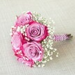 Resonating with the refined spirit of Stanmore weddings, this radiant rose bouquet is an emblem of both sophistication and heartfelt celebration. Central to the handheld arrangement are five resplendent roses, each carefully chosen for their mesmerizing two-tone petals-muted lavender and lilac blending into vibrant fuchsia at the outer edges for dramatic visual intrigue. These blossoms are interspersed with airy clusters of white gypsophila, their tiny blooms offering lightness and an almost whimsical texture throughout the rounded bouquet. The short stems are gathered and elegantly wrapped in deep plum satin, spiraling with graceful rows of pearlescent white beads, crafting a visually stunning handle and underscoring the bespoke nature of Stanmore's floristry. Subtle hints of the stems' natural green and brown are visible beneath, suggesting freshness and authenticity. Gently resting at a diagonal atop a softly textured, neutral linen surface, the bouquet's vibrant colours and sumptuous details draw the eye and capture the imagination. This floral composition is an ideal statement piece for a Stanmore bridesmaid, flower girl, or intimate anniversary, embodying both the artistry and warmth found in the area's celebrated floral traditions.