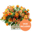 An opulent bouquet of orange and yellow flowers is showcased against a clean white background, the colours glowing with the easy warmth of a sunny day in Stanmore. Dominating the arrangement are several sumptuous orange roses, their petals opening in soft, velvety spirals that in some blooms fade gently to yellow at the centre, creating a natural, flame-like gradient. These are paired with bright yellow garden roses, tightly layered and perfectly round, adding a sense of classical beauty and careful structure. Threaded throughout the design, peach and light orange alstroemeria, also known as Peruvian lilies, bring a delicate, airy feel; their slender petals are lightly ruffled and decorated with fine stripes and speckles, giving the bouquet close-up interest and an almost painterly quality. Scattered among the softer forms, small spherical orange accent blooms stand out with their spiky, thistle-like texture, reminiscent of safflower heads; they inject a lively, contemporary energy into the arrangement and catch the light against the smoother petals. Surrounding the flowers is an abundance of greenery that enhances the warm tones and adds depth: broad, silvery-green eucalyptus leaves curve gracefully outward, while darker green foliage tucks between the stems, creating volume and a feeling of freshly gathered abundance. All the stems are nestled into a clear square glass vase, its sharp, modern lines and transparent sides showcasing the stems and water within, making the design feel clean and current, well-suited to a Stanmore living room or home office near Canons Park. Around the midpoint of the vase, a band of natural beige burlap or jute is wrapped smoothly, introducing a rustic, tactile contrast to the sleek glass. In the lower right corner of the image, a bold circular orange badge with crisp white capital letters announces VASE INCLUDED, clearly indicating that this joyful, autumn-inspired bouquet arrives exactly as pictured, ready to be placed on a table and enjoyed without any extra arranging.