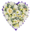 A carefully composed heart-shaped floral tribute set against a clean white backdrop, its surface densely layered with serene white, cream and pale yellow blooms that read as a quiet statement of remembrance. The composition is built around a single creamy-white rose at the center, its spiral of velvety petals acting as an anchor for the eye. Radiating outward are clusters of ruffled white carnations offering soft volume, and button-like white chrysanthemums with fine, spidery petals and gentle pale green centers that lend crisp texture. Smaller cream-hued spray roses and tight lisianthus buds nestle close to create depth, while tiny filler blooms and discreet pale-yellow touches brighten the palette without breaking the arrangement's solemn calm. Blue-green eucalyptus leaves weave through the blooms, their matte, silvery sheen giving a cool contrast and a faint herbal scent imagined by the senses. The entire heart is framed by a scalloped, deep lavender to rich purple ribbon that forms an elegant, respectful border and subtly heightens the visual dignity. Soft, indirect light in the photograph brings out petal translucence and the layered shadows between flowers, suggesting a tactile softness to the touch. As a florist's piece intended for funeral or memorial settings-often chosen by families here in Stanmore near Canons Park or along the Broadway-this cushion-like heart reads as an expression of enduring love and quiet consolation. The craftsmanship is evident in the balanced placement and dense packing of blooms: every petal and leaf placed to convey peace, reverence, and heartfelt sympathy for a service or remembrance.