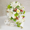 A luxurious, wedding-ready bouquet sits gracefully on a spotless white surface, framed by a softly textured beige background that could easily belong to a sunlit Stanmore reception room. The arrangement is dominated by open white Oriental lilies, their generous petals curling outward to reveal lightly speckled centres and golden stamens, giving a sense of fullness and intricate detail. Cradled among them, a single yellow rose forms a focal point, its creamy petals tightly layered in a perfect spiral that glows warmly amidst the cooler whites and greens. Scattered tufts of white baby's breath weave between stems, creating a gauzy halo around the larger flowers and softening the transitions between textures. Vivid green, cushion-like Green Trick dianthus add an unexpected twist, their mossy spheres standing out with a tactile richness that invites the eye to linger. Fine, feathery greenery extends from the heart of the bouquet, lifting the composition and creating a sense of organic growth that echoes the quiet, leafy streets around Stanmore Hill. Polished red hypericum berries are sprinkled thoughtfully throughout, their smooth, jewel-bright surfaces injecting lively colour that hints at festive gatherings or joyful anniversaries. Flowing down the right-hand side, a cascade of perfect white Phalaenopsis orchids tumbles elegantly, each bloom pristine with a subtle yellow flush at the centre, accompanied by a few unopened green buds that hint at blooms still to come. The entire arrangement is seated in a white woven basket or base, whose restrained, textured design is mirrored by two decorative white wicker spheres resting on the table to the left, bringing balance and a contemporary touch. This image captures a sophisticated floral composition ideal for weddings, engagement parties, or refined celebrations across Stanmore, lovingly styled with the eye of an experienced local florist.