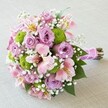 Delicately constructed by specialists in Stanmore's floristry, this compact and elegant bouquet presents a charming harmony of soft pinks, gentle lilacs, and vibrant greens-perfect for modern bridal moments or local celebrations. At the centre, plush roses bloom in shades of blush and lavender, their gently unravelled petals evoking love and gentle sophistication. Offsetting these are distinctive clusters of rounded, lime green chrysanthemums, reminiscent of Stanmore's leafy spaces in springtime. The arrangement is interwoven with trumpet-shaped pink Alstroemeria lilies, flecked with gold and cerise, and generously framed by clouds of white baby's breath, which drift between the blooms and soften the palette. Completing the design, deep green leaves peek beneath the petals, grounding the bouquet in nature's richness. The stems are snugly bound in a gleaming pink ribbon finished with lustrous white pearls, ready for a tender hand to hold them down a wedding aisle or present the bouquet as a thoughtful gift. Resting on a smooth, neutral surface, this fresh, stylish bouquet encapsulates the spirit of Stanmore's local artistry and is available for same-day delivery to celebrate life's most meaningful occasions.