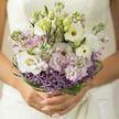 This bouquet appears as a piece of soft-spoken poetry held close to the body, an intimate cluster of bridal blooms that blend elegance with quiet emotion. At its heart, creamy white lisianthus unfurl in layered ruffles, their petals catching the light the way early sun sometimes glows across Stanmore's quiet suburban terraces. Between them, pastel lilac stock adds gentle height and a faintly sweet, nostalgic perfume, the kind that lingers in the air like a cherished memory. The base of the arrangement is encircled by rounded heads of lavender allium, each globe made up of tiny star-shaped florets that introduce playful, starlike texture. Tracing the outline of the bouquet, fine strands of deep green bear grass are twisted and looped into intricate curves, forming a graceful, modern halo that frames the softer shapes within. Scattered among the open blooms are a few tender green buds and pale stems, suggesting a story that is still unfolding, perfectly suited to a wedding day or engagement celebration. The bouquet is captured in natural light, which makes the whites shine clean and pure, while the lilacs and purples remain soft and understated rather than bold. You can almost feel the velvety petals and the cool, slightly damp stems, freshly conditioned as if they've just arrived from a morning delivery to a Stanmore florist near the Broadway. The mood is one of calm joy and expectation-the sort of bouquet a bride might carry through the leafy paths around Stanmore Country Park, its airy structure and flowing grasses moving gently with every step toward a hopeful future.