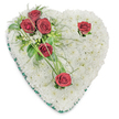 A tender, heart-shaped funeral tribute crafted entirely from a dense cushion of small, pristine white chrysanthemums, photographed against a clean white background. The chrysanthemums form a pillowy, textural surface that reads like a blanket of cloud-soft petals, their tiny faces turned outward to create an unbroken field of calm. From the upper left a diagonal spray of deep, velvety red roses sweeps down and inward: three rich roses clustered close together amid glossy green leaves and airy, fern-like fronds, with a few slender blades of bright green bear grass arching beyond them. Two solitary red roses punctuate the design-one nestled near the heart's upper right curve, the other resting toward the bottom point-each given a small halo of foliage so the crimson stands out against the white cushion. A thin emerald-green satin ribbon traces the heart's edge, its subtle sheen defining the shape and lending a composed, dignified finish. The overall palette of pure white, deep crimson and emerald green feels quietly ceremonial; the scent would be soft and clean with the faint, warm spice of roses when brought close. Soft overhead lighting casts gentle shadows that reveal the arrangement's depth and the florist's careful hand in placing each bloom for balance and repose. This is a classic sympathy piece meant to convey lasting respect and comforting presence at a funeral or memorial service. As a local florist in Stanmore I picture this tribute placed near a chapel in Bentley Priory or on a service table at Stanmore Broadway, where neighbours might recognise the timeless gesture of condolence it represents.