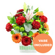 This joyful mixed bouquet is captured against a bright white background, its vivid colours and layered textures giving the impression of a celebration unfolding on a Stanmore dining table. The flowers are arranged in a sleek, rectangular clear glass vase, neatly dressed at the base with a light green and white gingham ribbon that softens the modern lines with a touch of country charm. At the centre, deep crimson red roses stand proudly, their velvety, tightly packed petals forming rich spirals that immediately draw the eye. Surrounding them are bright orange gerbera daisies, their broad, flat petals radiating from dark brown centres like small suns, adding a bold hit of energy and warmth. Tucked between these statement blooms are red-orange carnations, their frilled, ruffled petals giving the bouquet a plush, generous texture that feels abundant and welcoming. Rising above the central cluster, white oriental lilies provide graceful height; a few are fully open, revealing trumpet-shaped petals traced with subtle pink stripes and prominent stamens, while others remain as sleek, closed buds, suggesting continued unfolding beauty. Nestled among the larger flowers, small, spherical lime green pompom chrysanthemums bring a fresh, modern twist, their crisp colour and tidy shape punctuating the design with lively highlights. The arrangement is framed by layers of greenery-broad, dark green leaves and slender stems of silver-green eucalyptus-creating depth and a gentle, outward-curving silhouette that echoes the leafy calm of nearby Canons Park and local gardens. In the lower right corner of the image, an orange circular overlay partially covers the vase, bearing the bold white text VASE INCLUDED, clearly showing that this is a complete, ready-to-display gift. The overall mood is bright and celebratory, perfect for same-day delivery across Stanmore for birthdays, congratulations, or simply to lift someone's spirits.