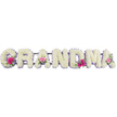 In this carefully arranged funeral display, the word GRANDMA appears in a line of generous letters, each one densely clothed in snow-white chrysanthemums. The chrysanthemums, with their small, radiating petals, are set closely together, forming a smooth, cushion-like surface that suggests softness and serenity. Outlining every letter is a fine ribbon of lilac, its pale purple hue and satiny texture adding a delicate frame that gives subtle definition and a sense of quiet refinement. The letters rest on a supportive base that is mostly hidden from view, much as they would when placed beside a coffin during a service in Stanmore or arranged for a final farewell near the town's leafy residential streets. At three thoughtful points along the word - the first G, one of the central As, and the ending A - small posies of pink blooms and foliage break the white expanse. Each miniature bouquet contains bright pink gerbera daisies, with bold centres and layered petals, paired with soft pink roses whose gently unfurling petals create romantic spirals. Slender sprigs and broader leaves of fresh greenery weave among the pink flowers, adding depth, contrast, and a hint of natural movement to the composition. The lighting is soft and controlled, illuminating every bloom evenly and highlighting the interplay between the crisp white chrysanthemums, the pastel ribbon edging, and the vivid yet tender pink accents. There are no distracting elements around the tribute; the focus stays completely on the floral lettering and the emotion it conveys. The arrangement feels like a deeply personal message of love and respect, created to honour a much-loved grandmother and provide a comforting focal point for family and friends in their time of remembrance.
