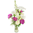 A vase of quiet celebration: slender white calla lilies rise like sculpted porcelain trumpets, their pale yellow spadices delicate against glossy white petals. The arrangement is built around a vertical spine of tall white stock, its dozens of clustered florets lending soft texture and a gentle, upward rhythm that guides the eye. Bold, magenta peonies provide dramatic contrast - two fully open blooms sit in the lower half with ruffled, velvety petals that catch the light, while a smaller, tightly furled bud on a visible stem promises another bloom soon. A creamy white rose nestles near the base, its compact spiral of petals offering a classic counterpoint to the peonies' exuberance. Wisps of Gypsophila (baby's breath) are threaded throughout, their tiny white stars creating an airy, cloud-like backdrop that softens the composition. Lush greenery - a mix of slender, fern-like fronds and broader glossy leaves - frames the bouquet, deepening the colour contrast and giving the display a garden-fresh feel. The stems sit in a gently curved clear glass vase; the water and visible stems add an uncomplicated honesty to the design and a hint of cool morning light. This is an arrangement that reads as both modern and romantic: suitable for a birthday celebration, Mother's Day, or a thoughtful anniversary gift. As a local floral piece, it would feel at home on a dining table in Stanmore or as a heartfelt delivery to a neighbour off Stanmore Broadway, carrying the kind of attentive care you expect from experienced florists in the area.