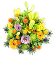 Presented against a clean white backdrop, this lush, mounded bouquet reads like a sunlit corner of Stanmore Common: bright and exuberant yet thoughtfully composed. Radiant yellow Asiatic lilies thrust upward, some fully unfurled with their speckled petals and elegant stamens exposed, while others remain slender, chartreuse-yellow buds that promise more blooms. Warm orange Gerbera daisies fan their flat, sunshine-hued petals around darker centres, paired with playful globes of small orange-and-golden-yellow button blooms that give the arrangement a textured, almost confetti-like rhythm. Soft lavender-purple roses nestle quietly among the louder tones, their spiralled petals offering a cool, romantic counterpoint and a gentle, powdery scent that seems to float from the bouquet. Cushion-like lime-green button chrysanthemums fill the hollows with ruffled, mossy texture, creating generous volume and a verdant cushion for the focal flowers. Cool, architectural blue-grey thistles - likely Eryngium - push from the lower edges, their spiky bracts adding an unexpected, modern contrast and a touch of coastal steel-blue against the warm palette. A variety of glossy and matte green foliage unifies the composition, their different leaf shapes and tones giving depth and natural movement as if a light breeze were passing across a Stanmore market stall on a late-spring morning. The overall mood is celebratory and comforting - suitable for birthdays, a bright 'get well' message, or as a vibrant sympathy tribute - and demonstrates skilled floral layering and attention to proportion, texture, and scent that a local florist would craft with care for neighbours around Stanmore High Street and Canons Park.
