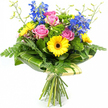 A lively, hand-tied bouquet of pink, yellow, and blue blooms is photographed in full length against a stark white background, allowing each flower and leaf to stand out with clarity, much like a display in a well-lit Stanmore florist window. At the centre, several pink roses unfurl softly, their petals delicate and velvety, creating a romantic focal point that suggests affection and care. Nestled alongside them, bright yellow gerbera daisies with pronounced dark brown centres bring a playful, uplifting touch, their circular, daisy-shaped blooms radiating warmth that would brighten any home from Stanmore station to the quiet residential streets nearby. Reaching up from within the bouquet, tall blue delphinium stems introduce elegant height, their clusters of small florets lending a cool contrast that balances the warmth of the roses and gerberas. The arrangement is richly cushioned by an assortment of greenery. Feathery fern fronds spill gracefully from the edges, giving the bouquet a gentle, natural softness, while broad, glossy tropical leaves with faint lighter streaks are carefully folded and wrapped around the base of the flower heads to form a smooth green collar. Nestled between these are tufts of bright green, textured filler foliage that add depth and visual interest, filling the bouquet so that it appears generous and abundant from every angle. Slim, light-green stems tipped with tiny buds emerge above the main blooms, adding a sense of movement and new growth. The stems themselves are gathered neatly at the bottom, secured with a pale cream or soft green wrap and a simple bow, leaving the trimmed stems visible in a classic hand-tied style. The overall mood is bright, fresh, and celebratory - a versatile bouquet that would serve beautifully as a birthday surprise, thank-you gift, or centrepiece for a family gathering in Stanmore.